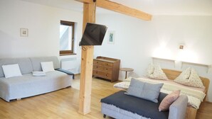 A modern bedroom with a wooden ceiling, a grey sofa, a bed with multiple pillows, and a small wooden dresser. - Family vacation home with 6 studio apartments. (Ceský Jiretín)
