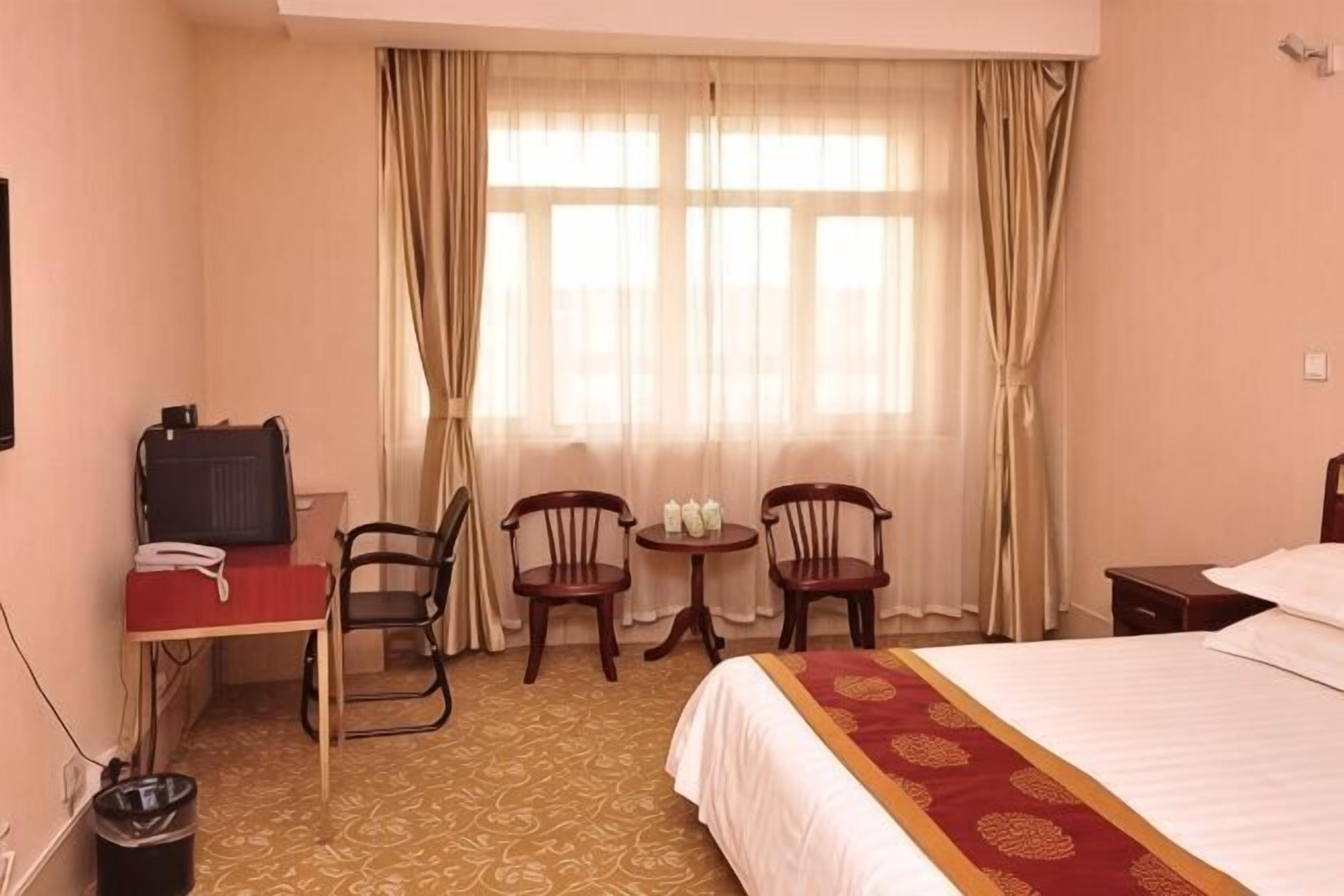 Habitación de hotel con cama, escritorio con teléfono, dos sillas, una mesita con tazas y una ventana con cortinas.