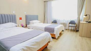 A hotel room with two beds, a small table, a chair, and a desk with a lamp.