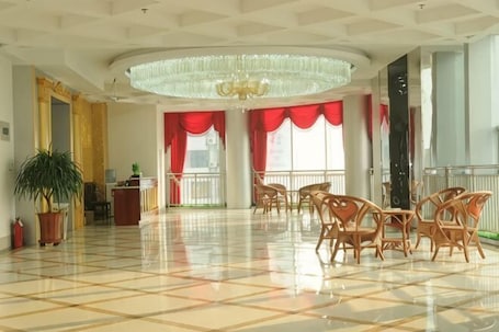 A spacious lobby with a checkered floor, a chandelier, red curtains, and a potted plant.. Bailong Hotel