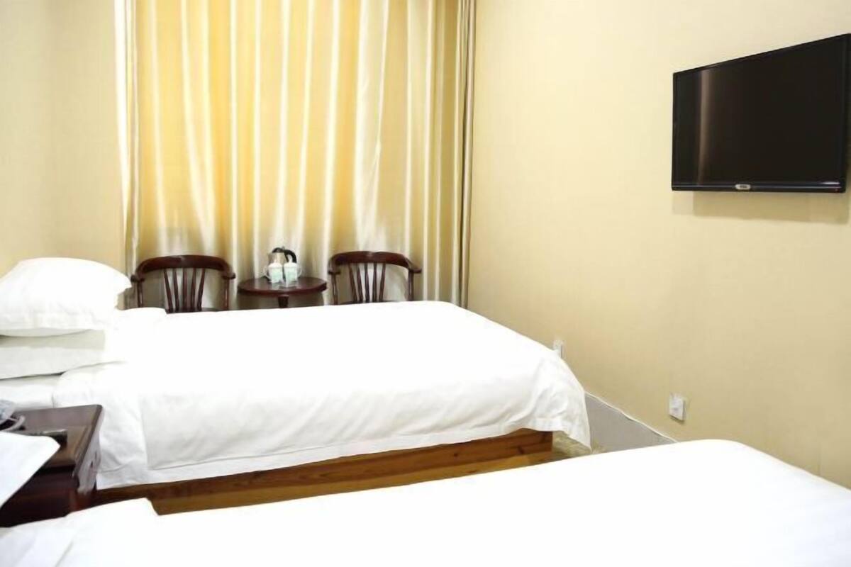 A hotel room with two beds, a television mounted on the wall, and a window with curtains.