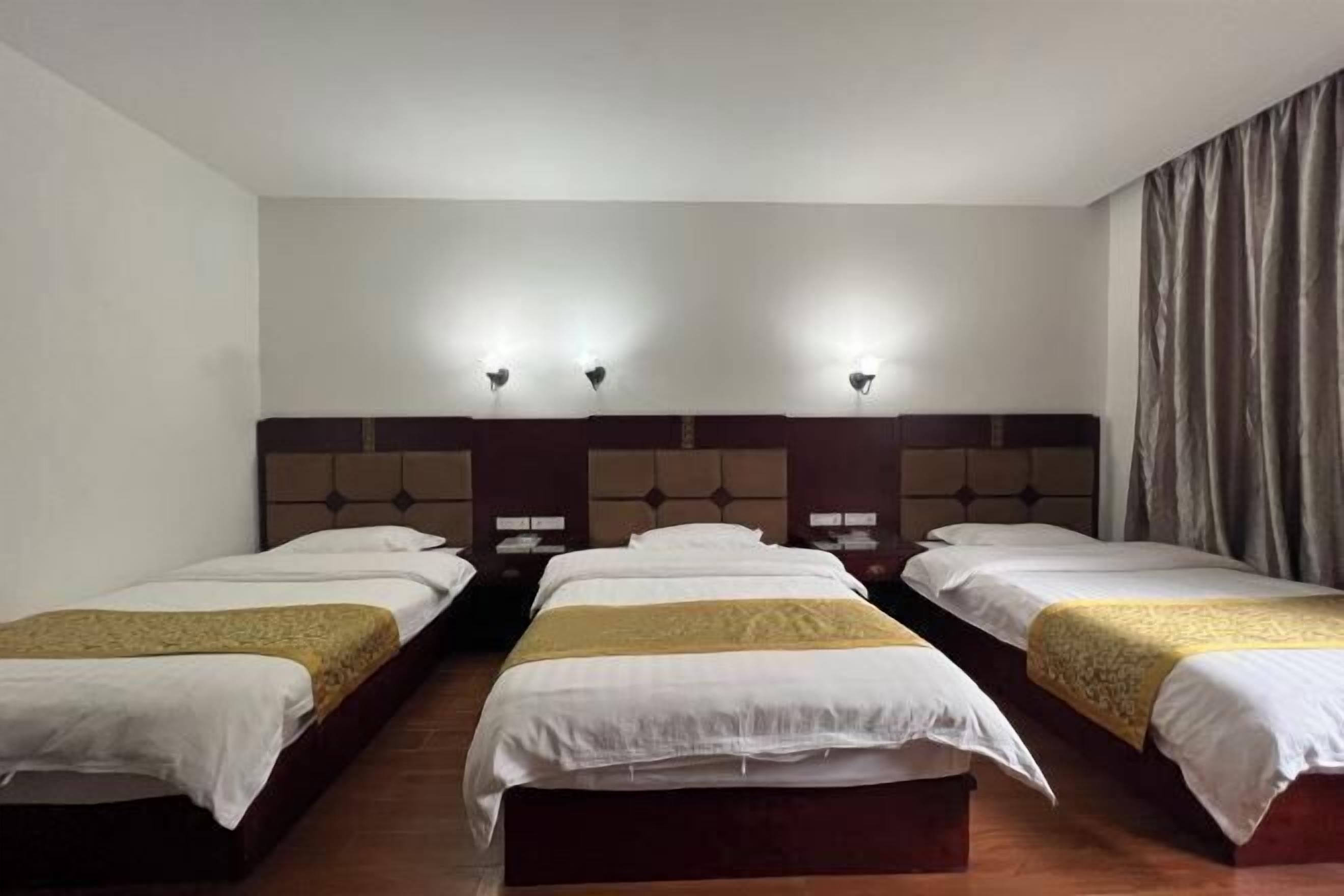 Une chambre d’hôtel avec trois lits simples, chacun doté d’une tête de lit et de tables de chevet.