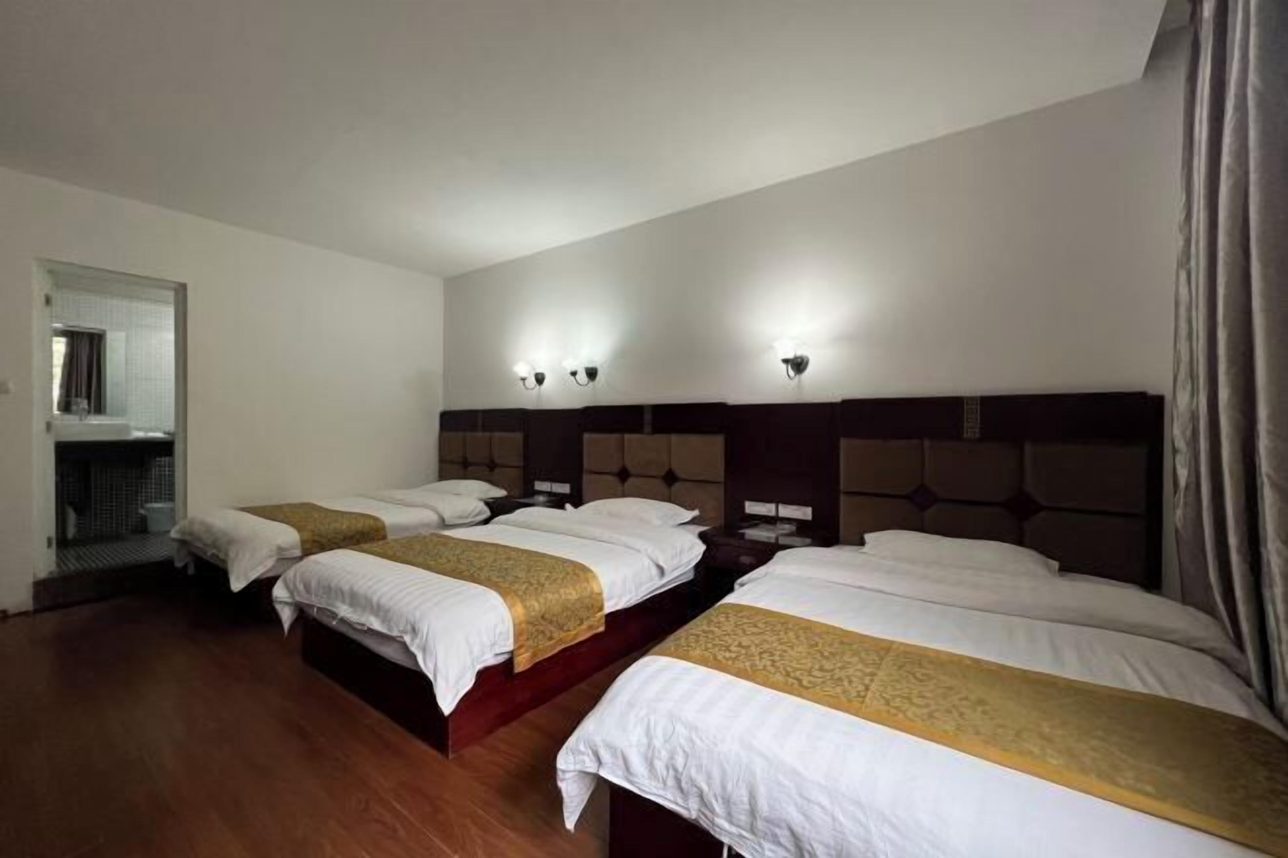 Une chambre d’hôtel avec quatre lits disposés en rangée, chacun étant muni d’une tête de lit et de tables de chevet.