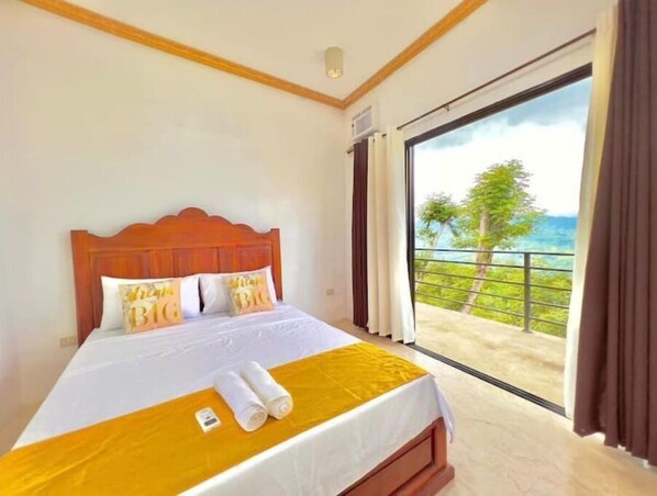 Relax in this serene room with a large bed, ocean views, and a balcony overlooking lush greenery.