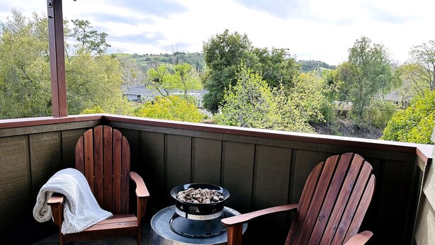 A wooden deck with two Adirondack chairs and a metal fire pit.