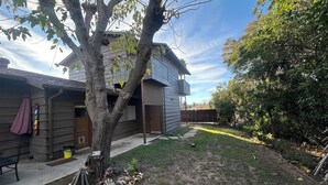 A residential backyard with a wooden house, a tree, and a fenced area.