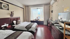 Een hotelkamer met twee bedden, een bureau met een televisie, een raam met gordijnen en uitzicht op buiten.