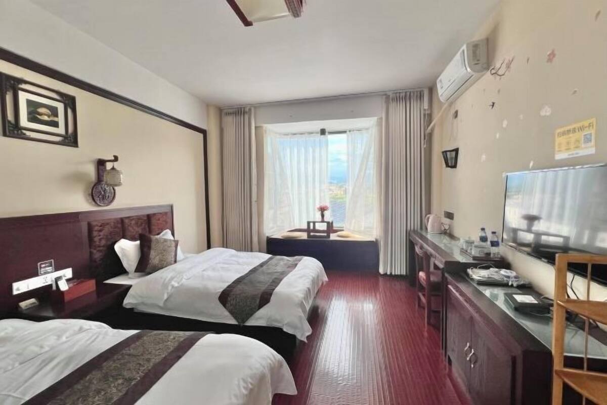 Une chambre d’hôtel avec deux lits, un bureau avec une télévision, une fenêtre avec des rideaux et une vue sur l’extérieur.