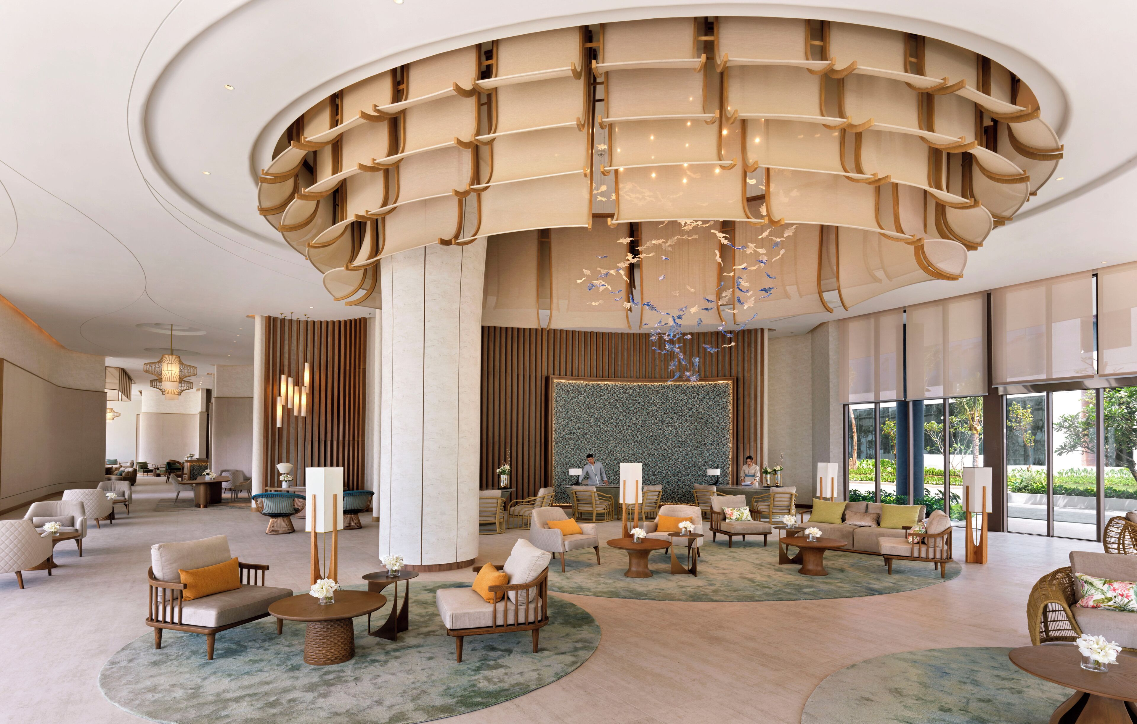 A spacious lobby with multiple seating areas, a large decorative ceiling structure, and a view of the outdoors through large windows.