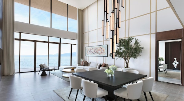 A spacious living area with a large dining table, comfortable seating, a large window with a view of the sea, and a potted tree. - Villa Le Corail, A Gran Melia Hotel (Bac Nha Trang)