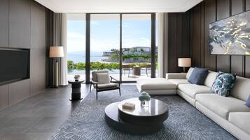 A modern living room with a large flat-screen TV, a sofa, a coffee table, and a view of a pool and mountains.