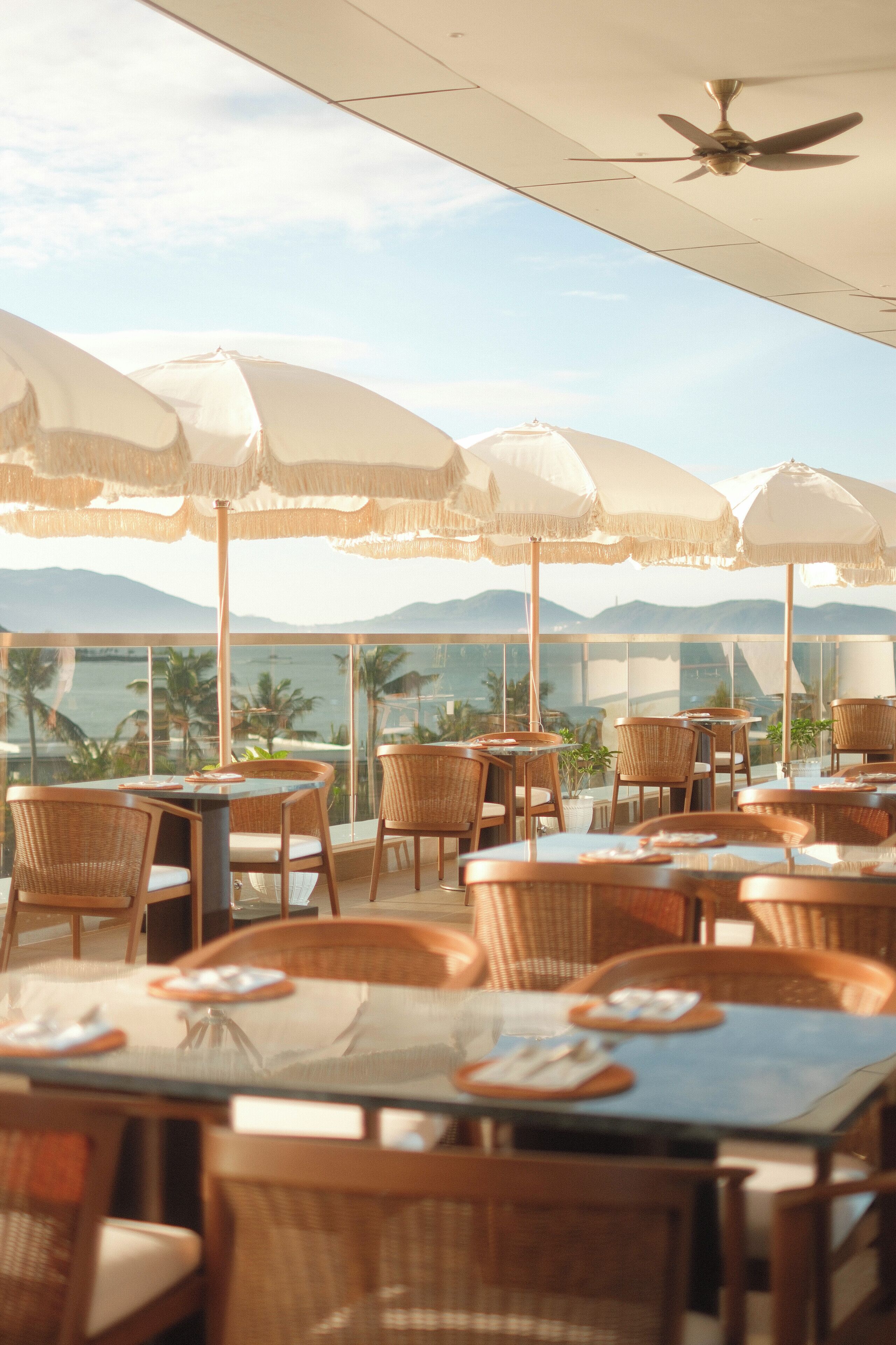 Restaurant al terrat amb taules i cadires sota paraigües, amb vista panoràmica a les muntanyes i al mar.