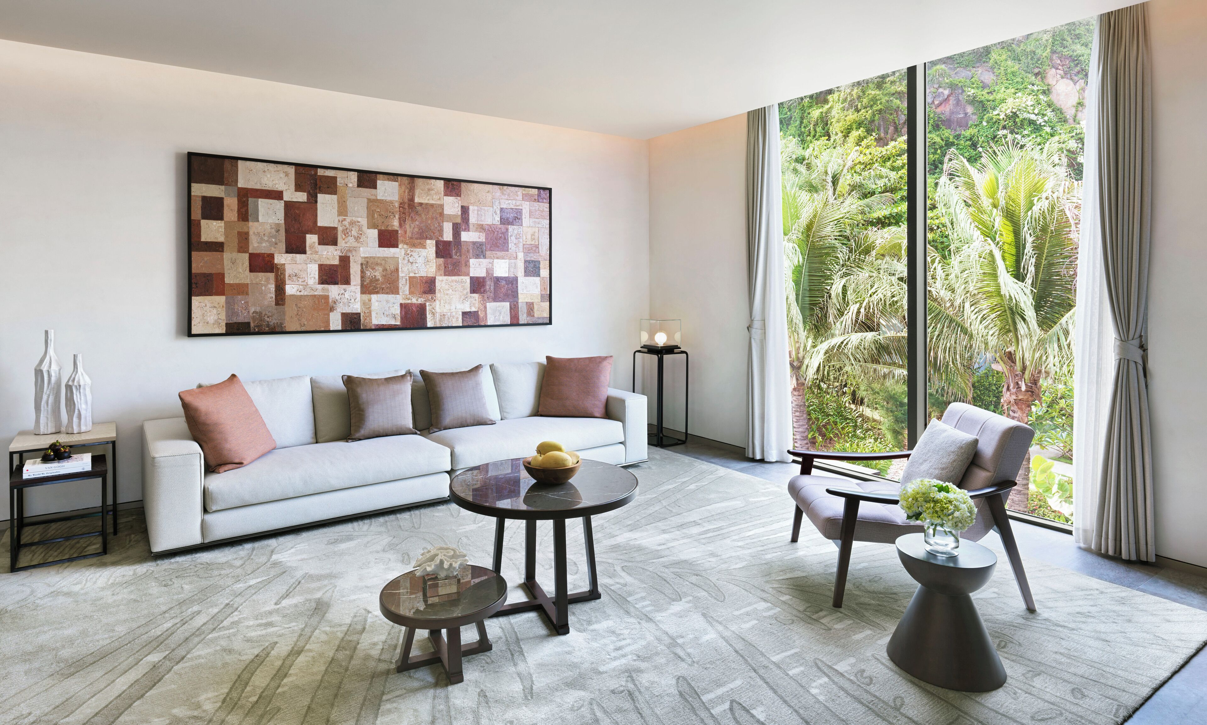 Una sala de estar moderna con un sofá, dos sillones, una mesa de centro y una lámpara de pie. Un cuadro abstracto de gran tamaño decora la pared, y una ventana ofrece vistas a exuberante follaje.