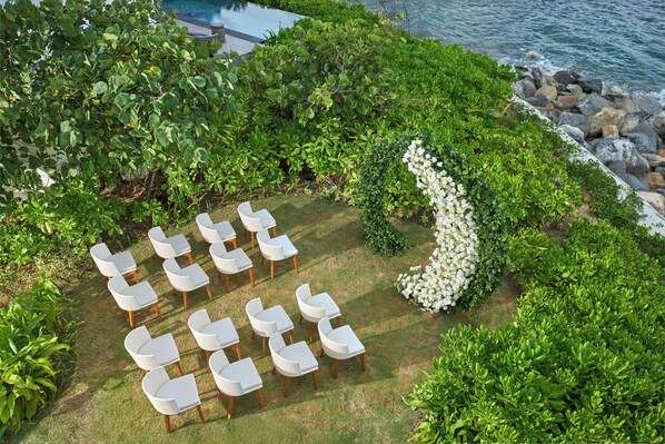 An outdoor seating area with white chairs and tables arranged on a lawn, surrounded by lush greenery and a white flower arrangement. - Villa Le Corail, A Gran Melia Hotel (Bac Nha Trang)
