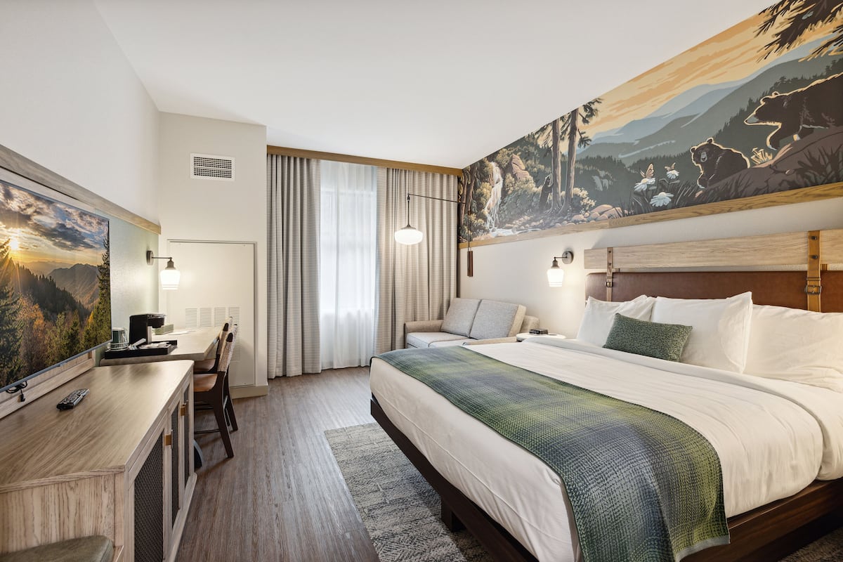 A hotel room with a large bed, a desk with a chair, a television, and a painting on the wall.