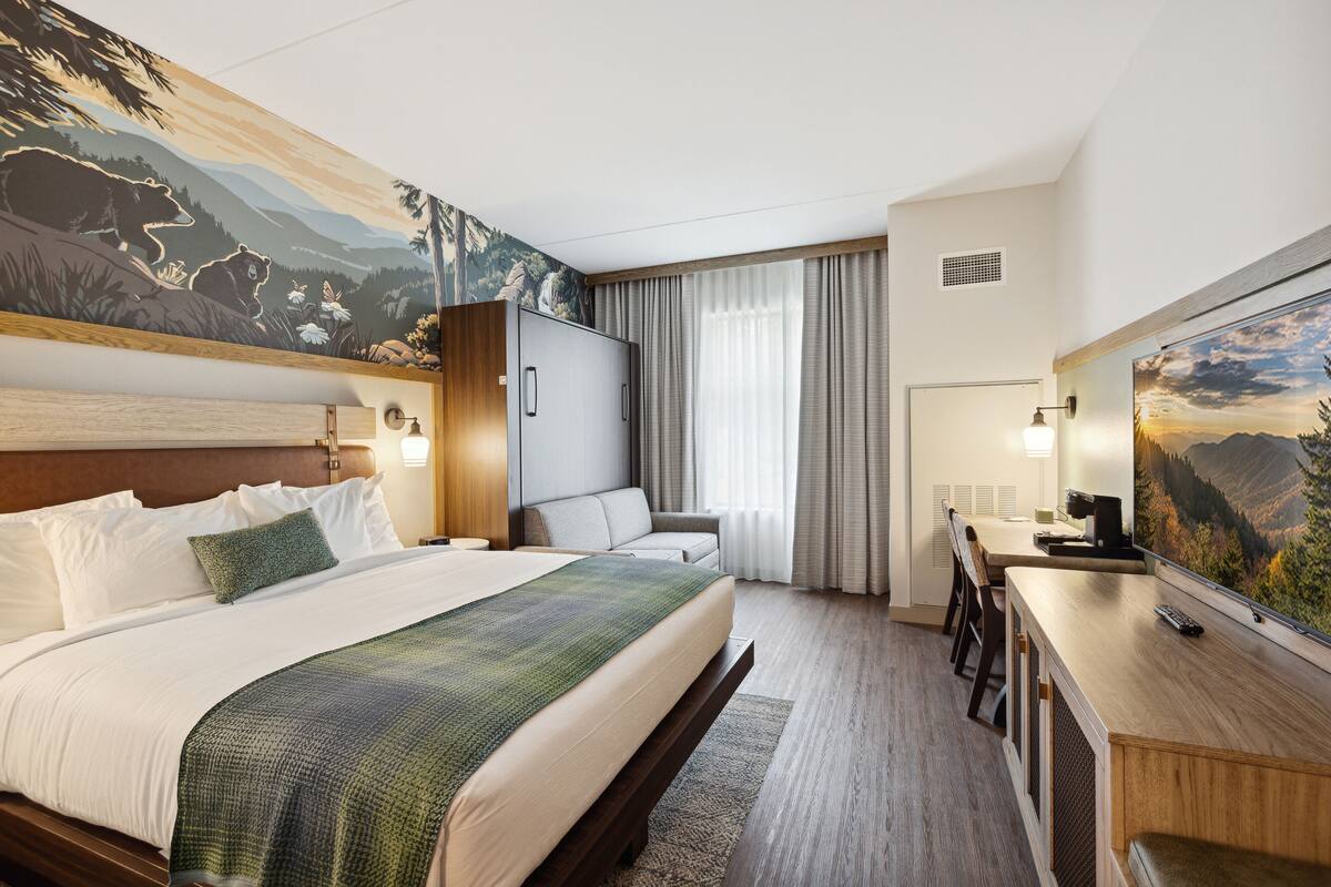 A hotel room with a large bed, a desk with a chair, a television, and a painting on the wall.