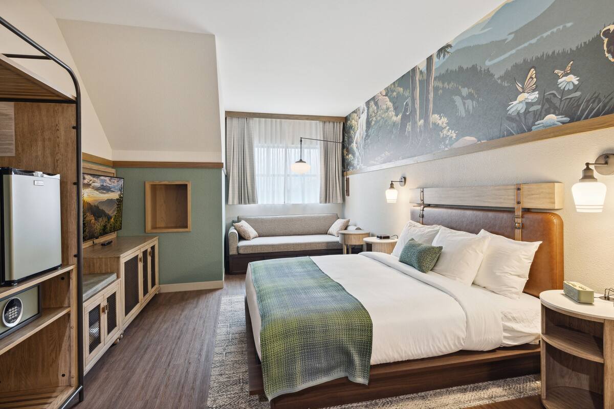 A hotel room with a large bed, a sofa, a desk, and a refrigerator.