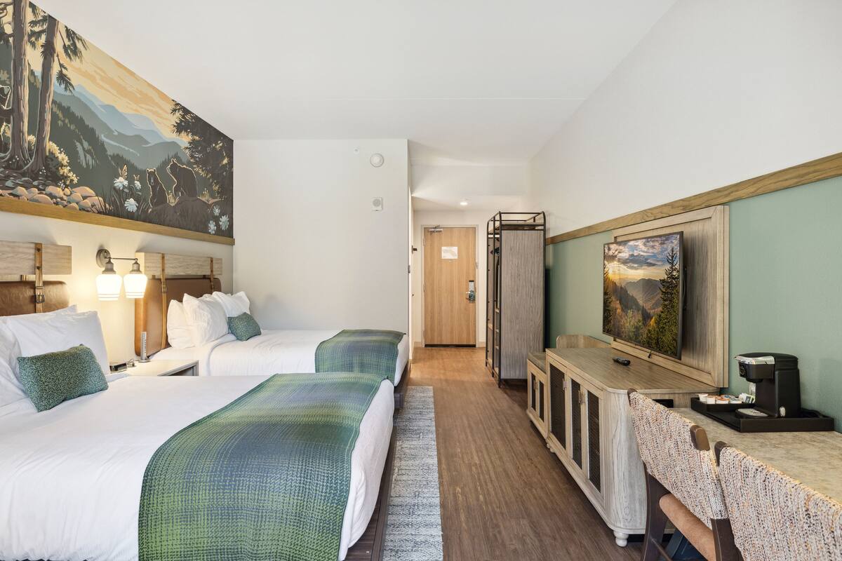 A hotel room with two beds, a desk with a coffee machine, a painting, and a door leading to another room.