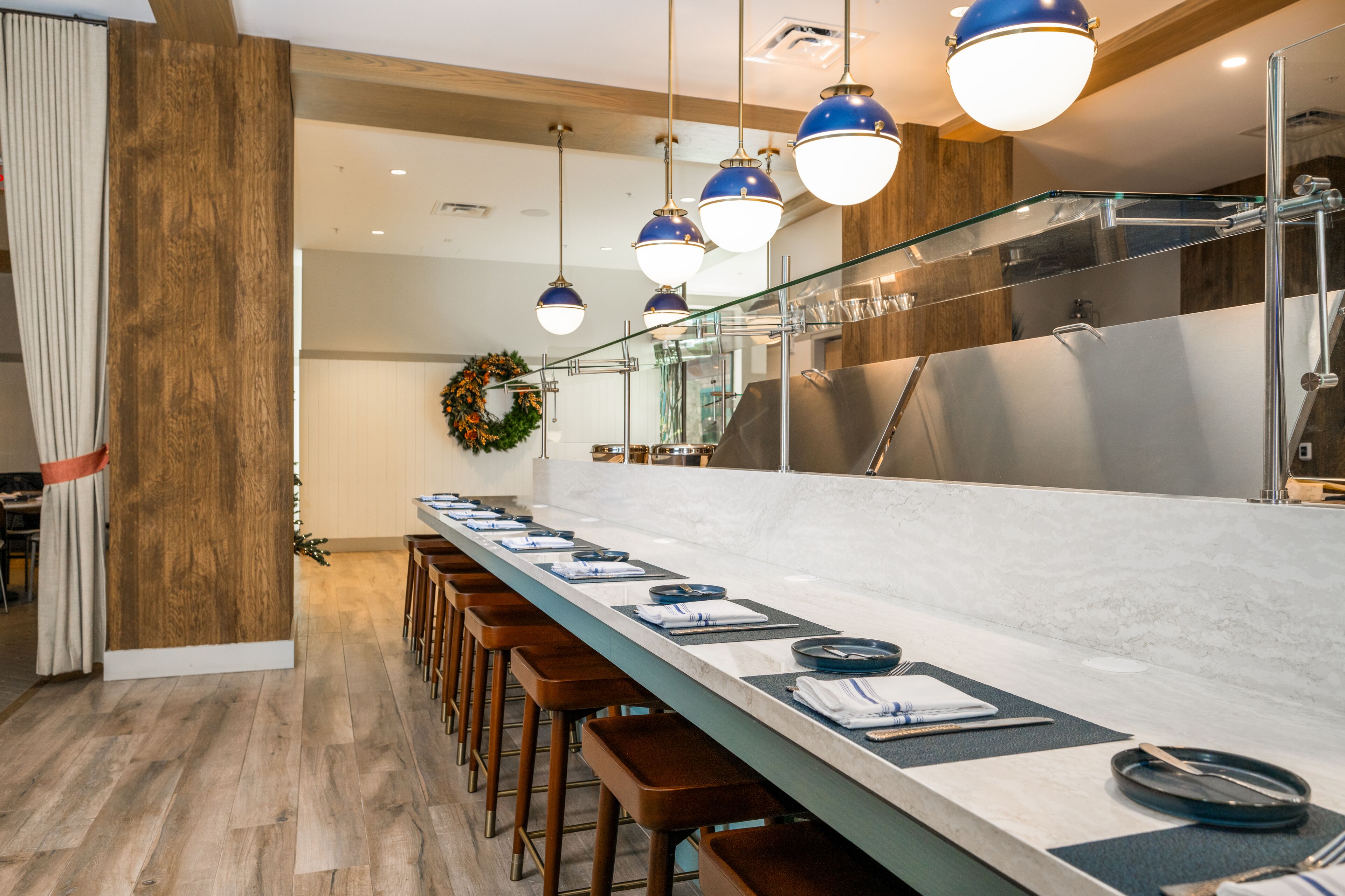 A modern kitchen with a long counter, bar stools, and pendant lighting.