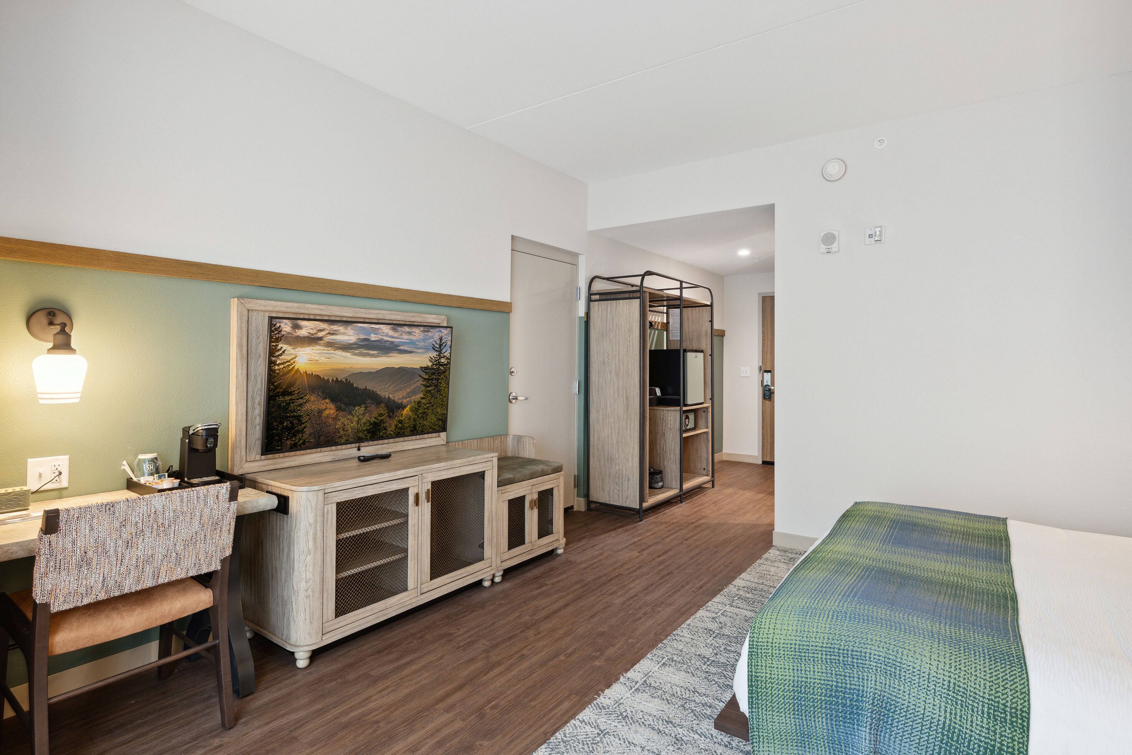Habitación de hotel con cama, escritorio, silla, televisor y armario.