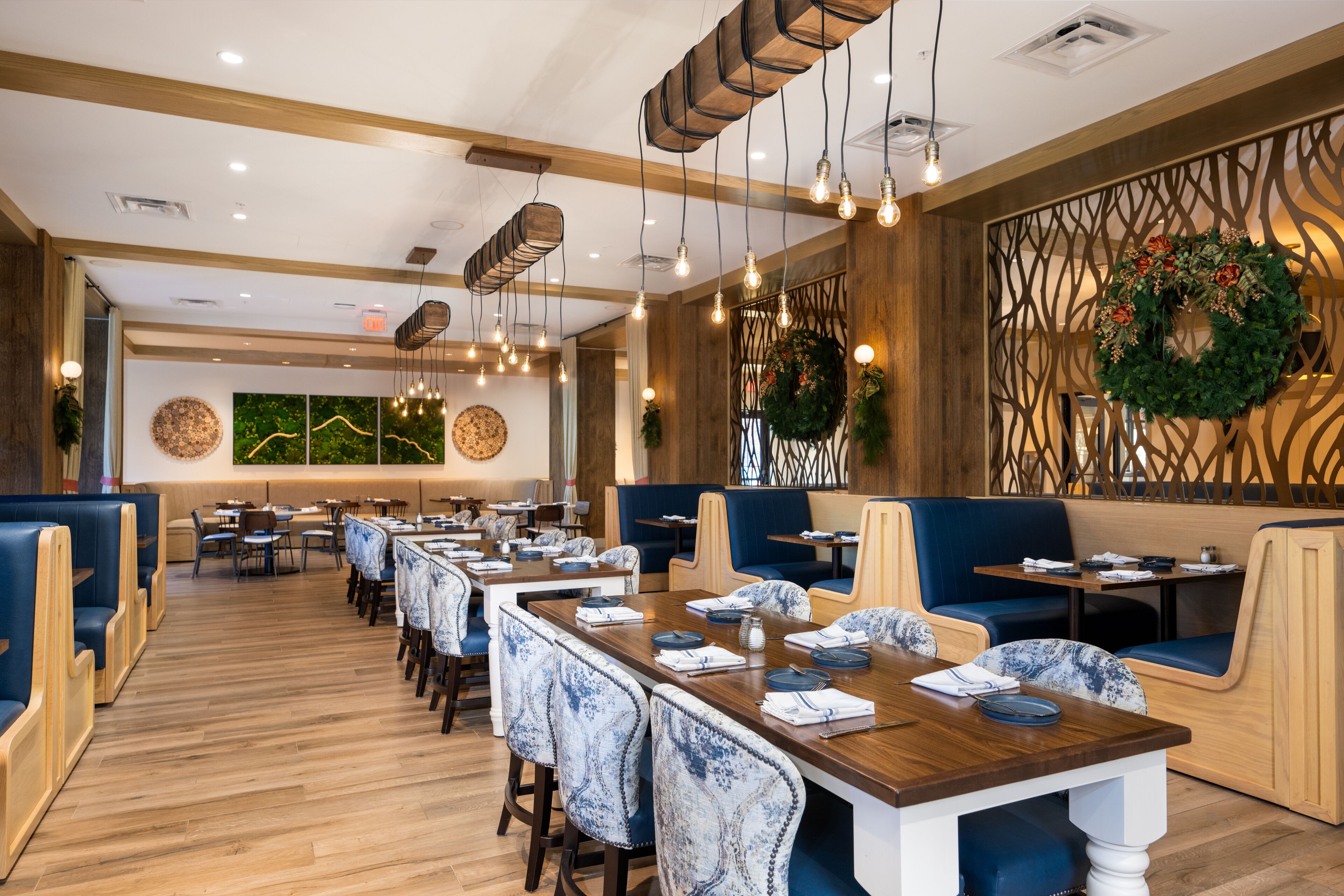 A restaurant with wooden tables, blue upholstered booths, and hanging light fixtures.