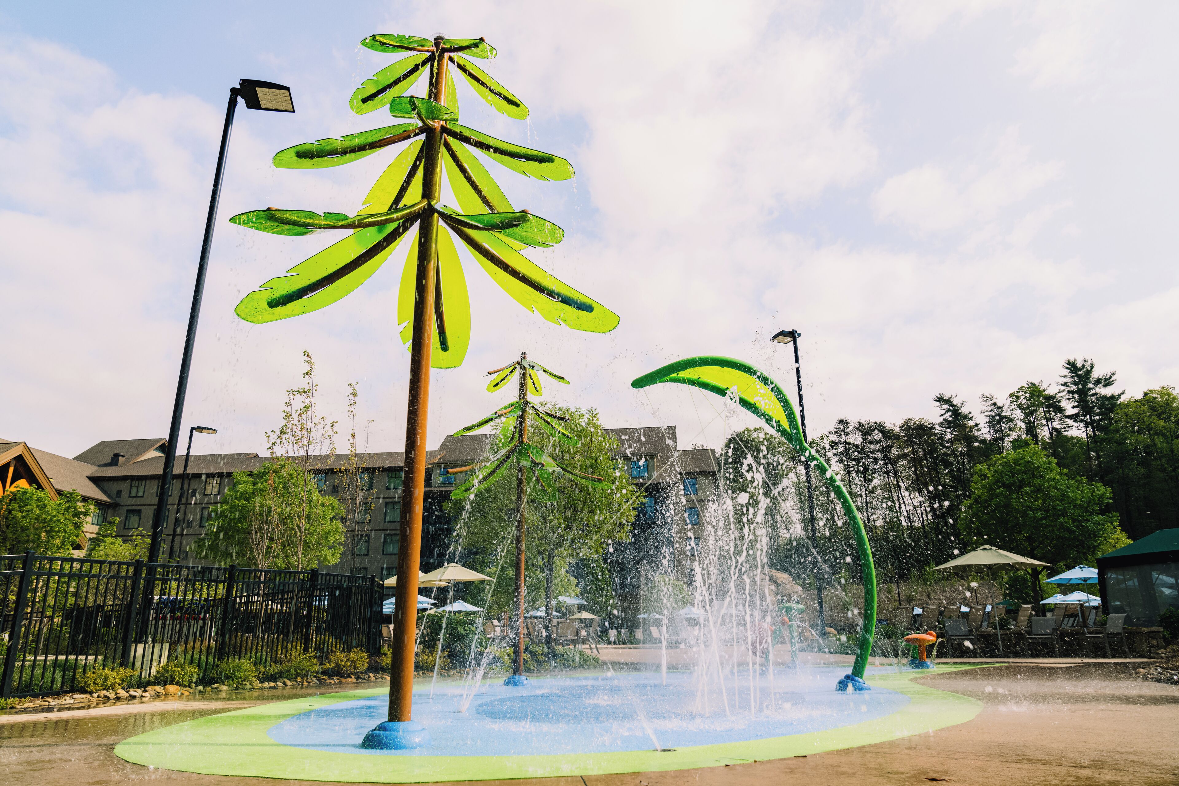 Una fuente de agua con un diseño singular, rodeada de una zona pavimentada y una valla.