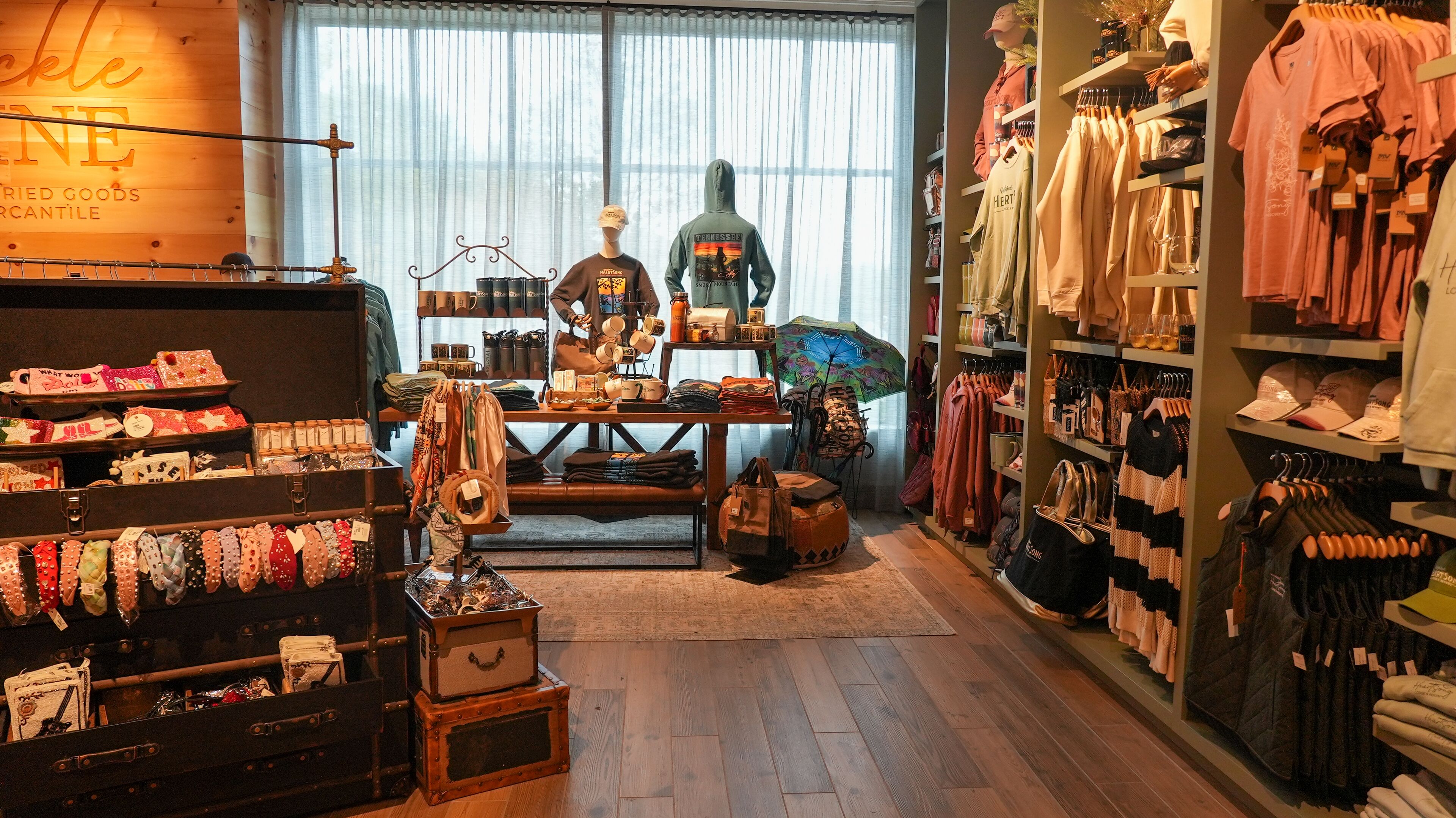 A boutique store with wooden flooring, shelves of clothing, and various accessories.