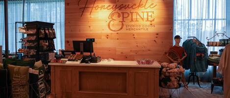 Un acogedor interior de tienda con una pared de madera que muestra 'Honeysuckle Pine' y 'STORIES GOODS MERCANTILE'. Estantes con varios artículos y un maniquí al fondo.