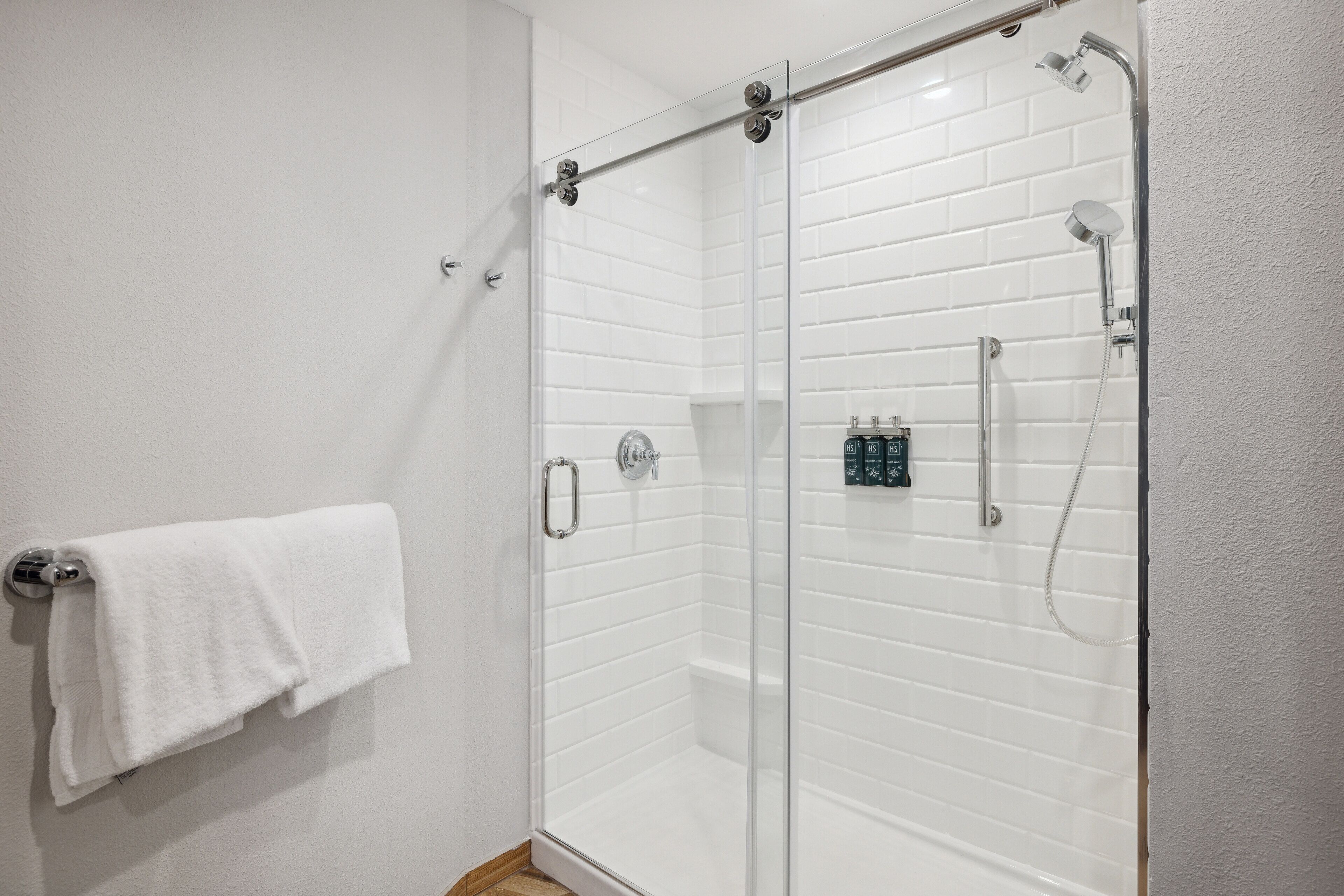 A glass-enclosed shower with white tiled walls, a towel rack, and a control panel.