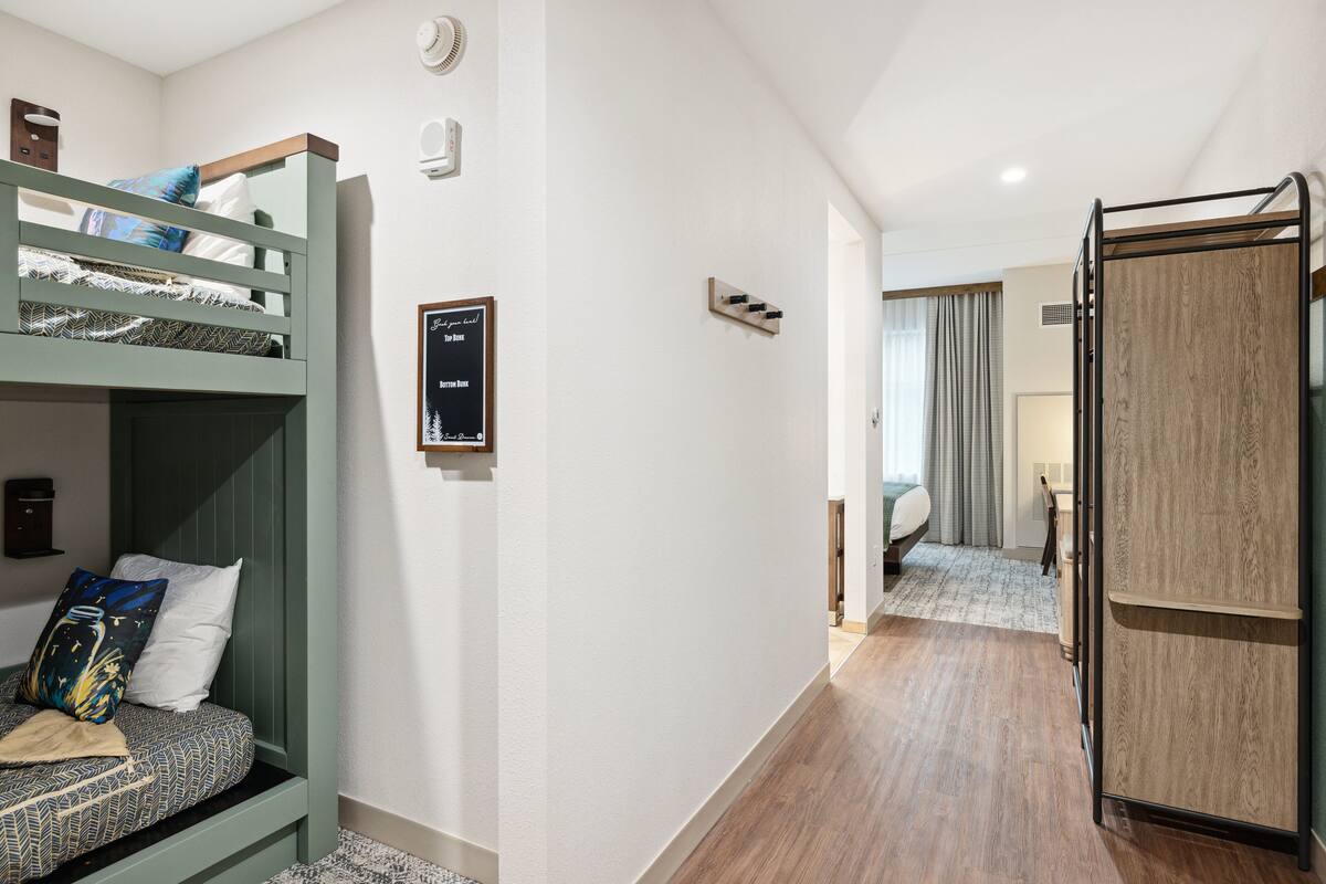 A bunk bed with a patterned mattress, a small shelf, and a framed sign on the wall.
