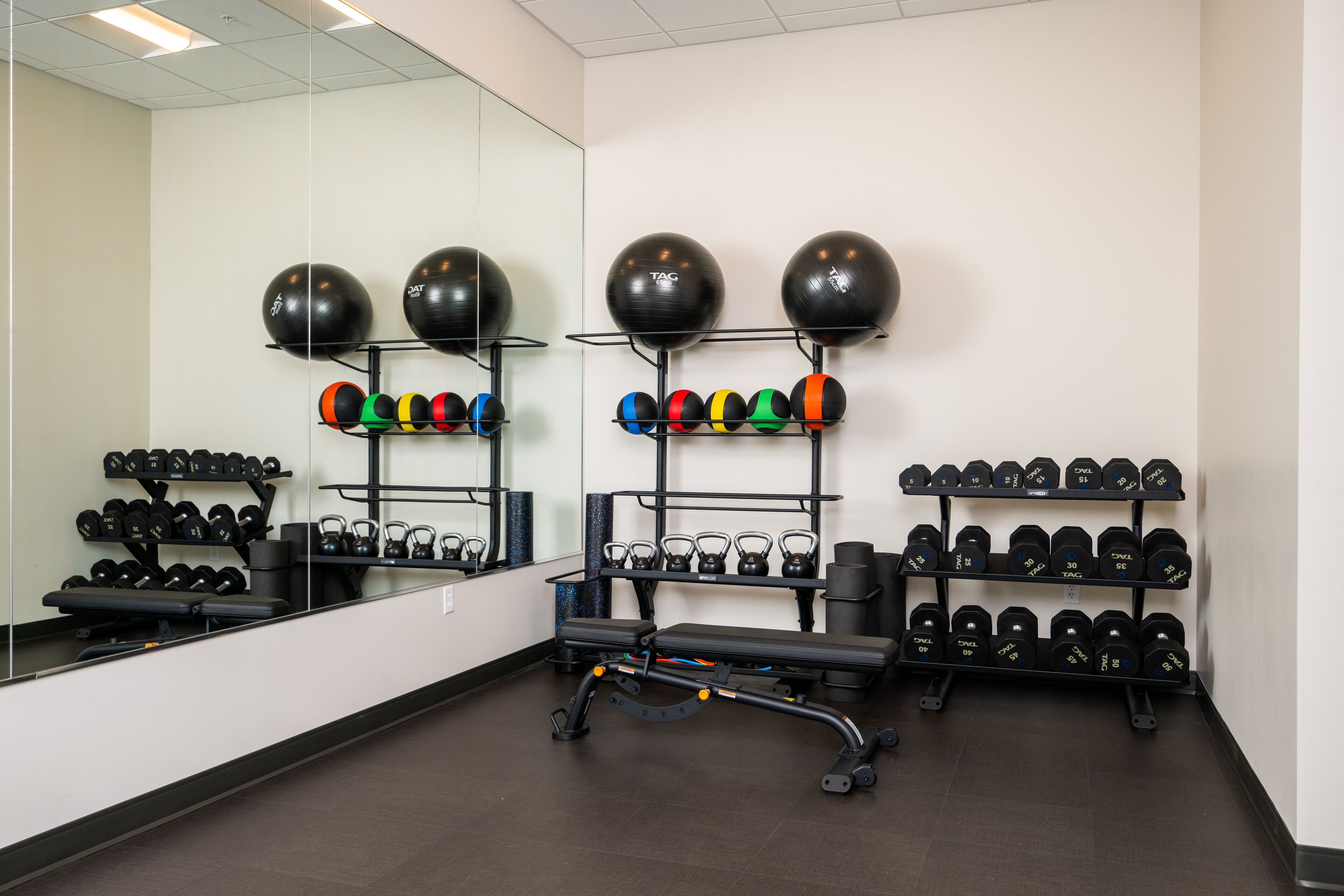 Academia com equipamentos de ginástica, incluindo halteres e kettlebells, e um banco.