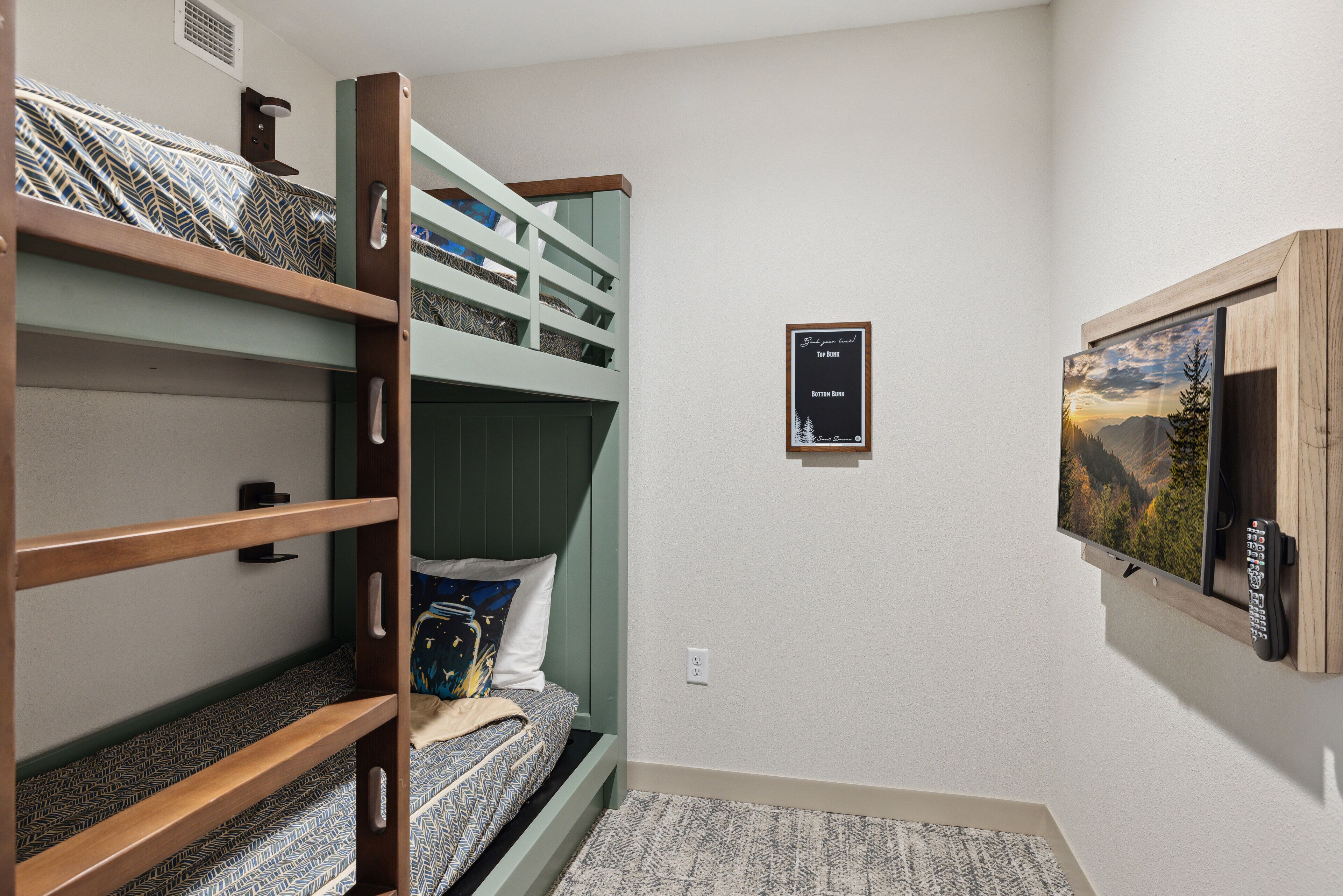 A room with bunk beds, a mounted TV, and a framed picture on the wall.