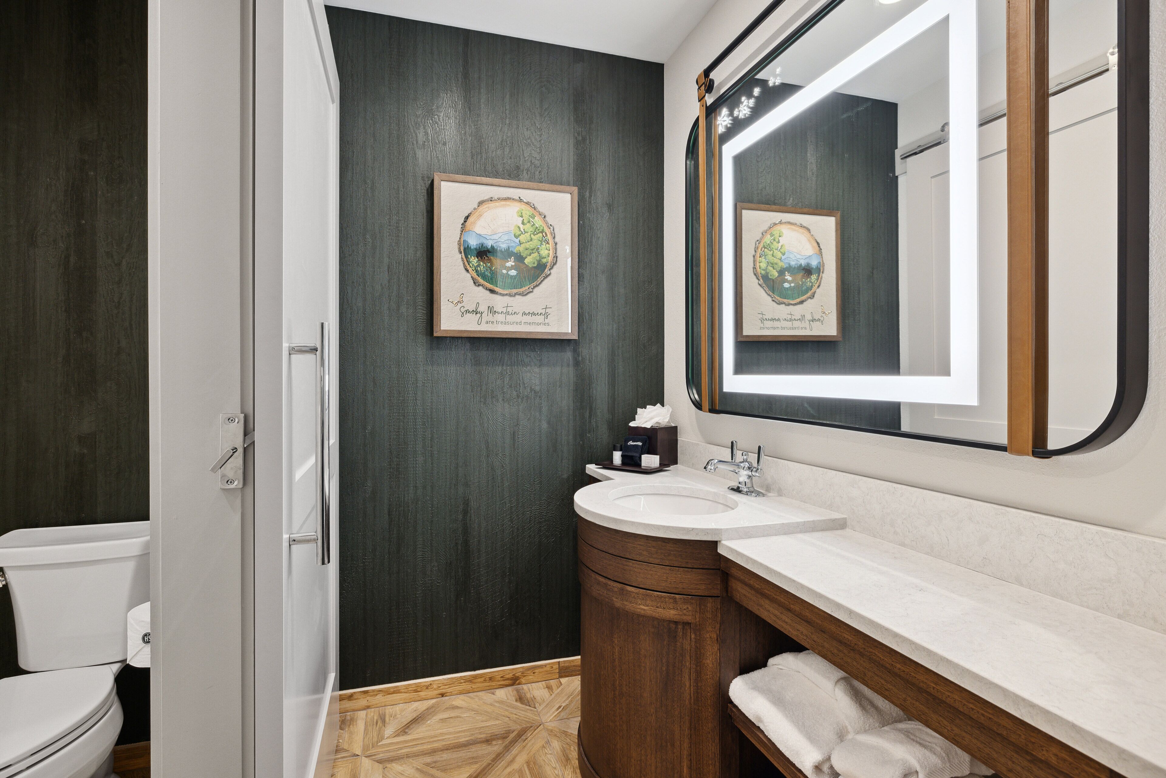 A modern bathroom with a toilet, sink, and vanity. There are framed pictures on the wall and a mirror above the sink.