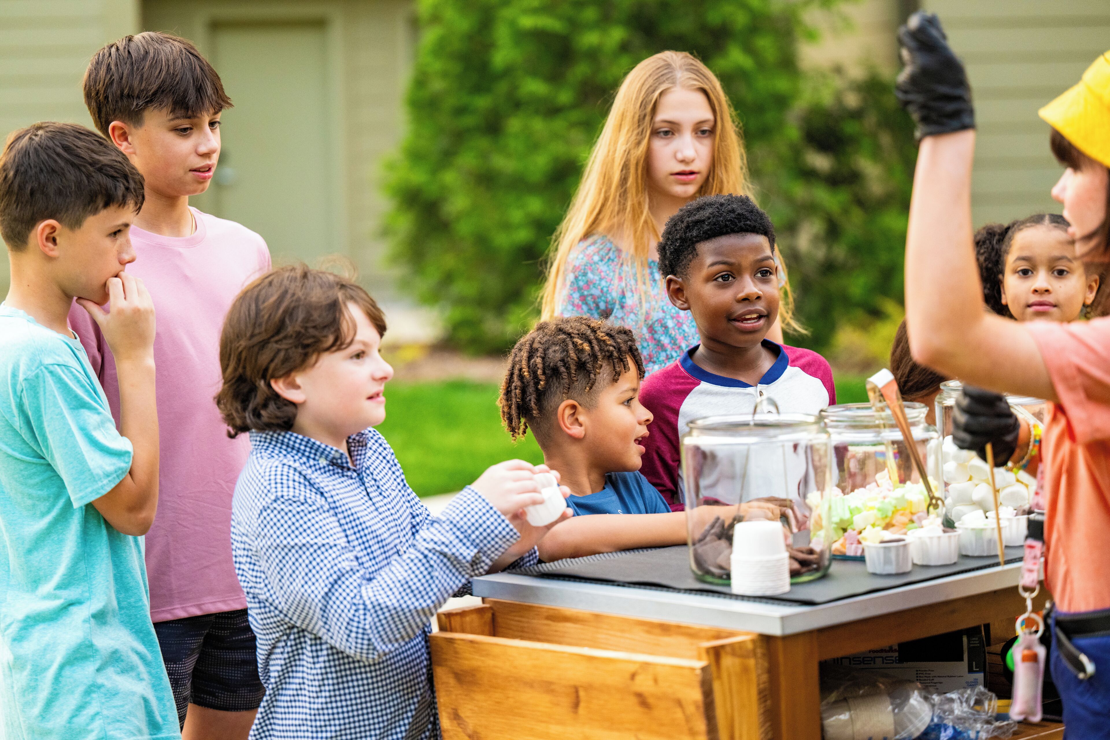 A group of children gathered around a table with various items, possibly for a craft or cooking activity.