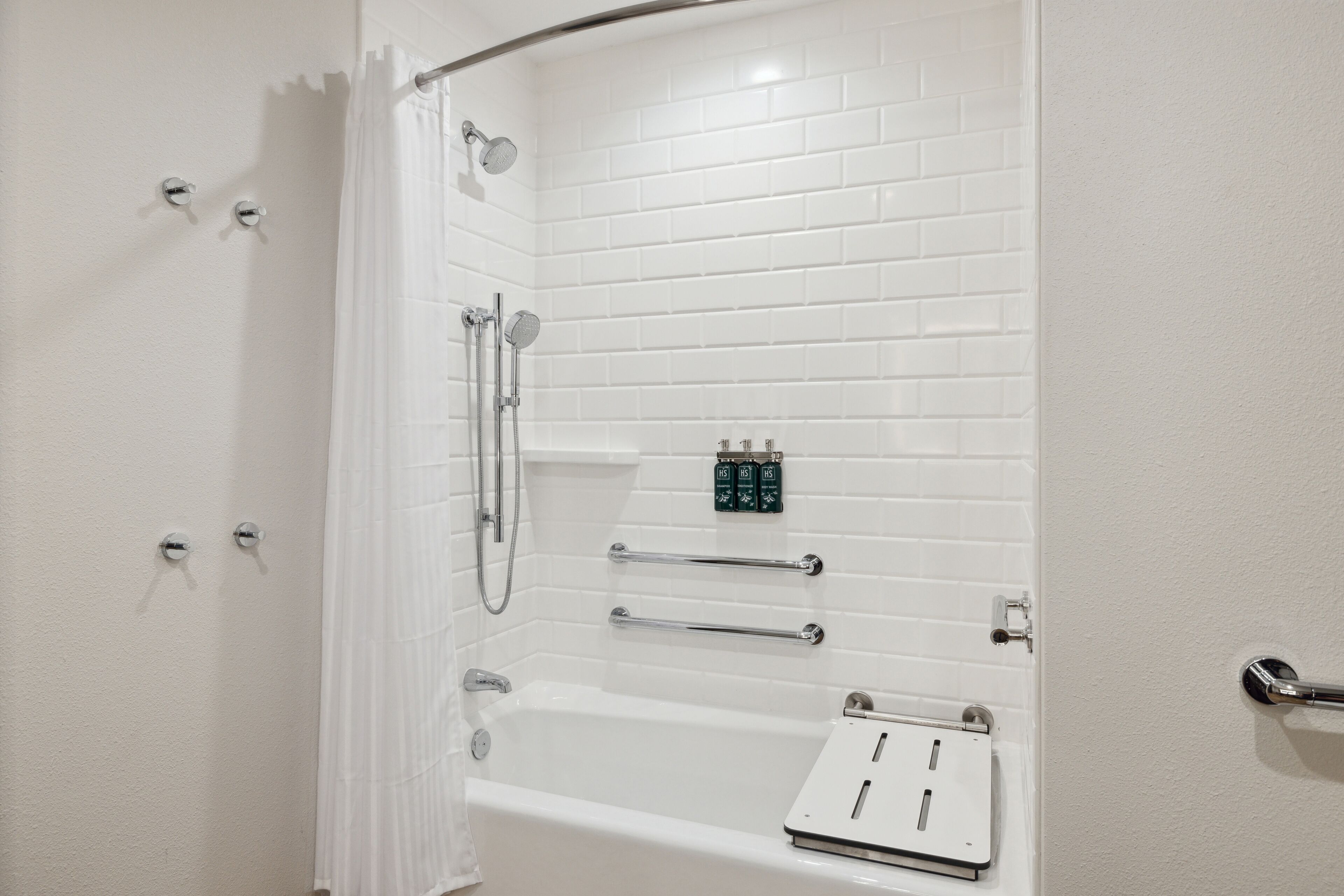 Un box de ducha con azulejos blancos, un panel de control, barras de apoyo y un cabezal de ducha manual.