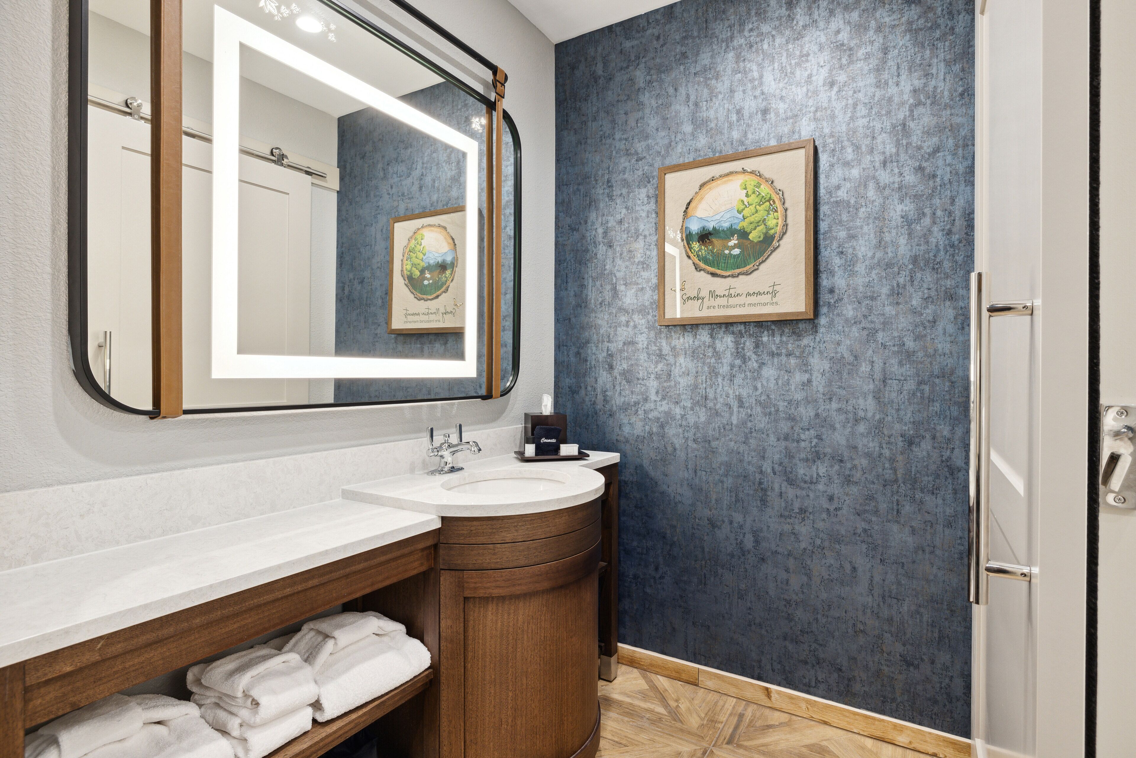 A bathroom with a large mirror, a sink, and a framed artwork on the wall.
