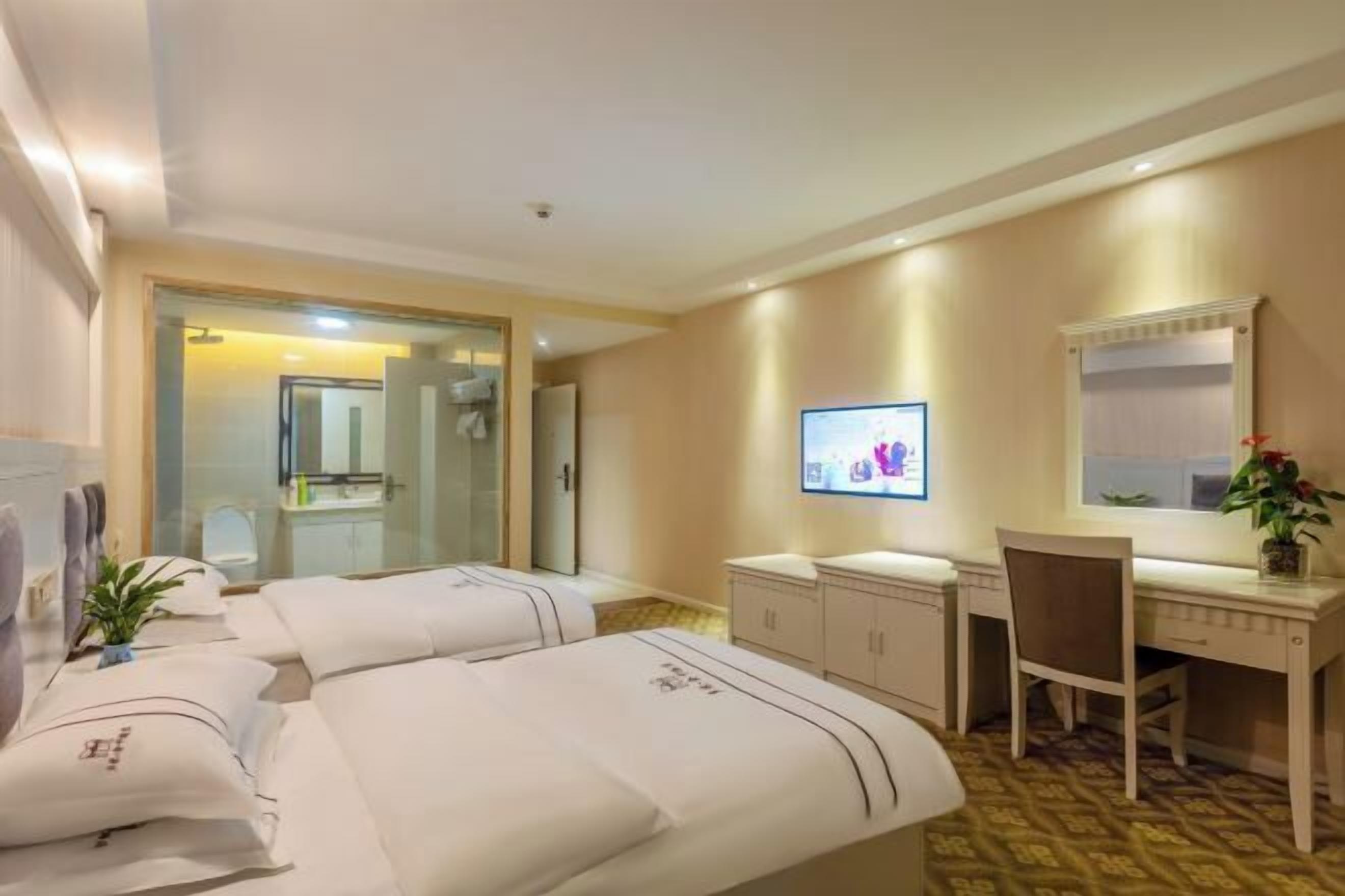 A hotel room with two beds, a desk, a chair, a television, and a bathroom visible through an open door.
