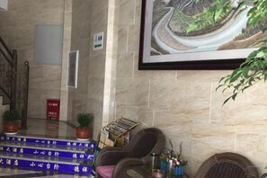 Eine Lobby mit Marmorwand, einem gerahmten Landschaftsbild, einem Empfangstresen mit Zeitschriftenständer und einer Treppe.