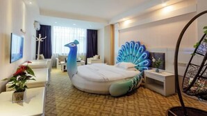 A modern hotel room with a unique peacock-themed bed, a flat-screen TV, a desk with a plant, and a seating area with a sofa and chairs. - Duomi Chain Hotel (Lijiang Ancient City) (Lijiang)