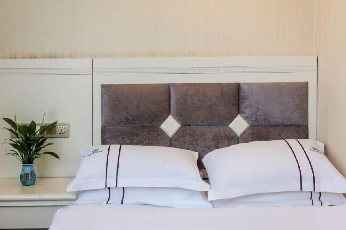 A hotel room with a bed, white pillows, a small plant, and a decorative headboard.