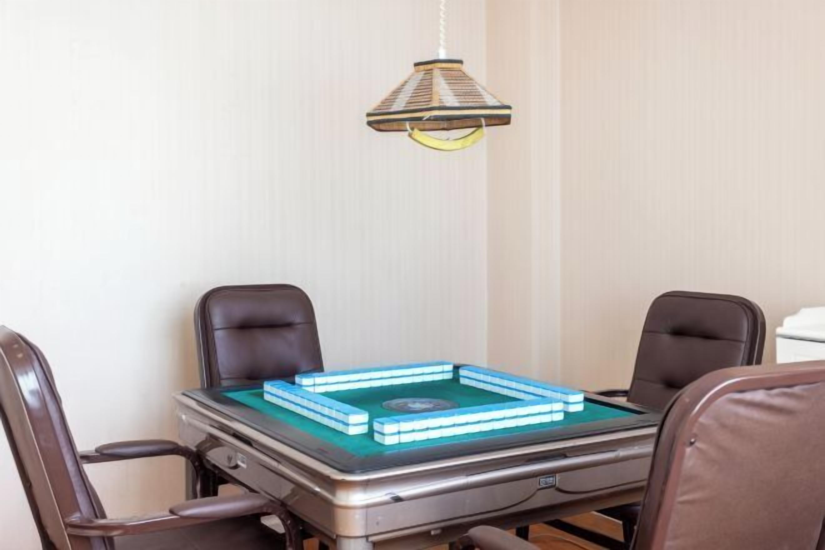 Une pièce comprenant une table de billard, quatre chaises, une lampe suspendue et une petite table recouverte d’un drap de feutre vert.