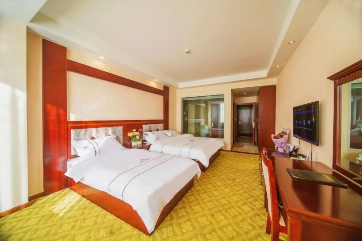 A hotel room with two beds, a desk, a TV, and a bathroom visible through an open door.