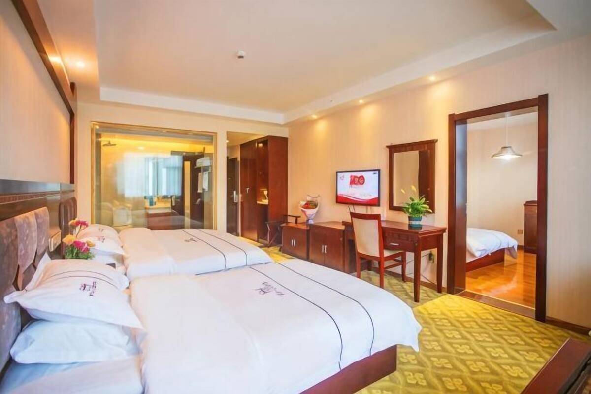 A hotel room with two beds, a desk, a chair, a TV, and a mirror.
