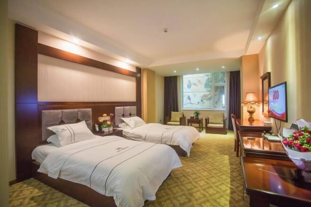A hotel room with two beds, a desk, a TV, and a window with a view.