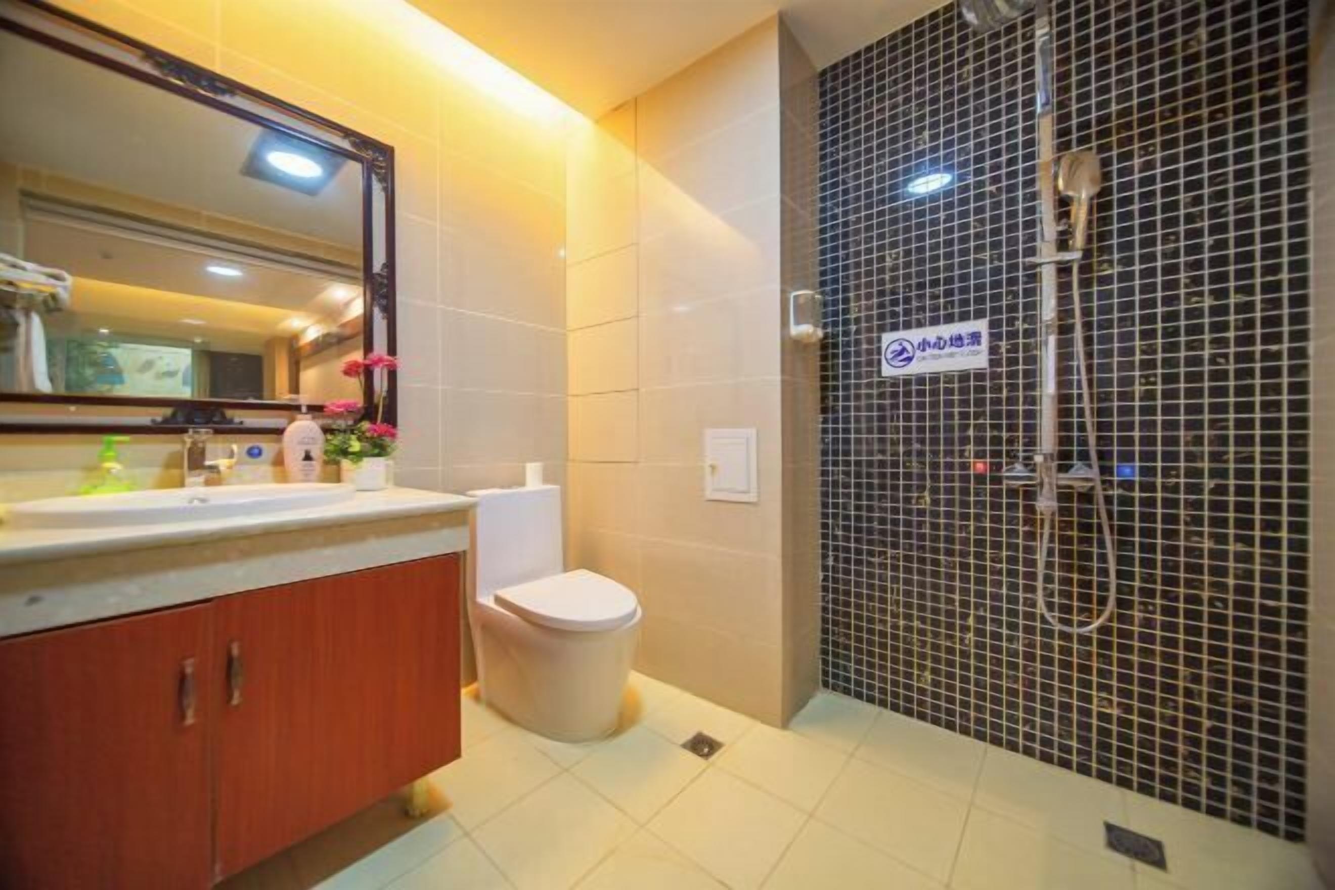 A bathroom with a sink, mirror, toilet, and shower area.