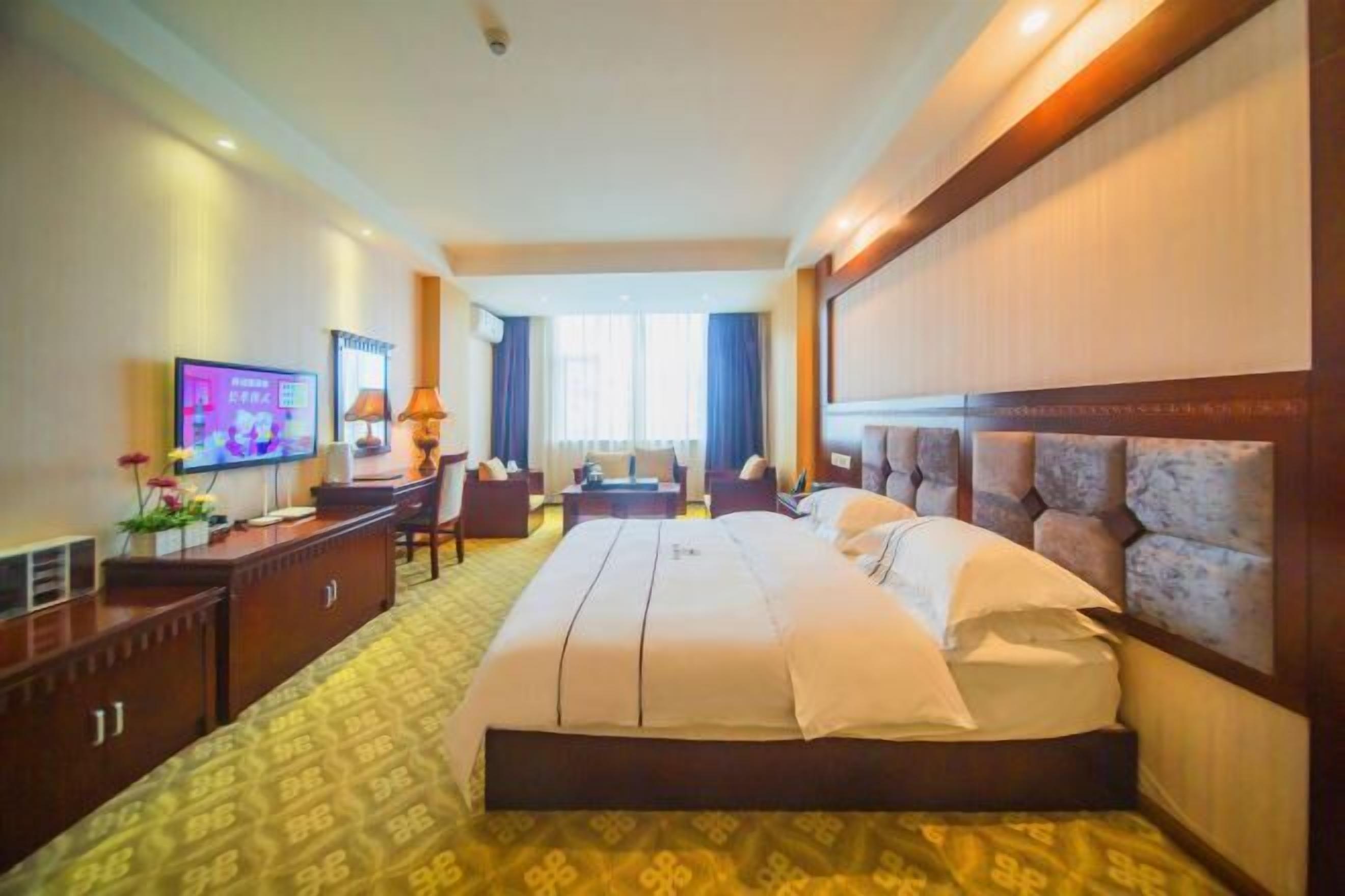 Una camera d'albergo con un letto grande, una scrivania con televisore e un angolo salotto con sedie e un tavolo.