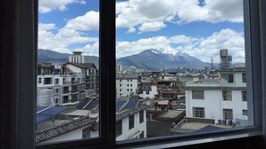 A view through a window of a cityscape with traditional buildings, a mountain range, and a clear sky. - Duomi Chain Hotel (Lijiang Ancient City) (Lijiang)