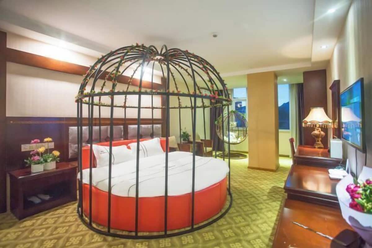 A hotel room with a circular bed, a large window, a desk, and a television.