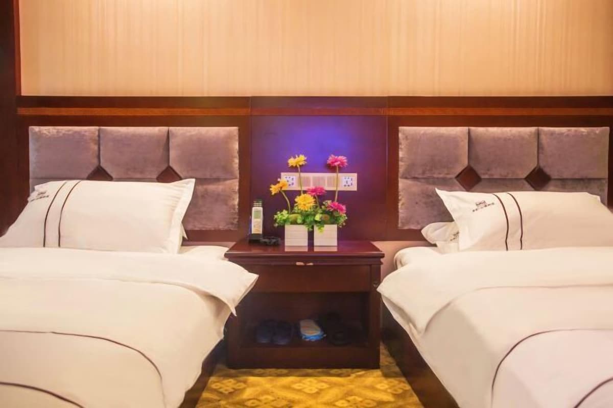 A hotel room with two beds, a nightstand with a vase of flowers, and a wooden headboard.