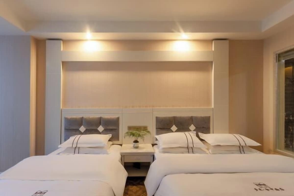 A hotel room with two beds, a nightstand with a plant, and a large window.